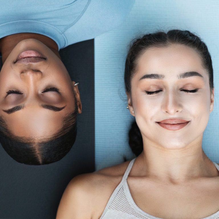 Calm glad young arabic and african american women athletes with closed eyes practice yoga, breathing exercises on black and white mat. Lifestyle, sports, fitness and workout together